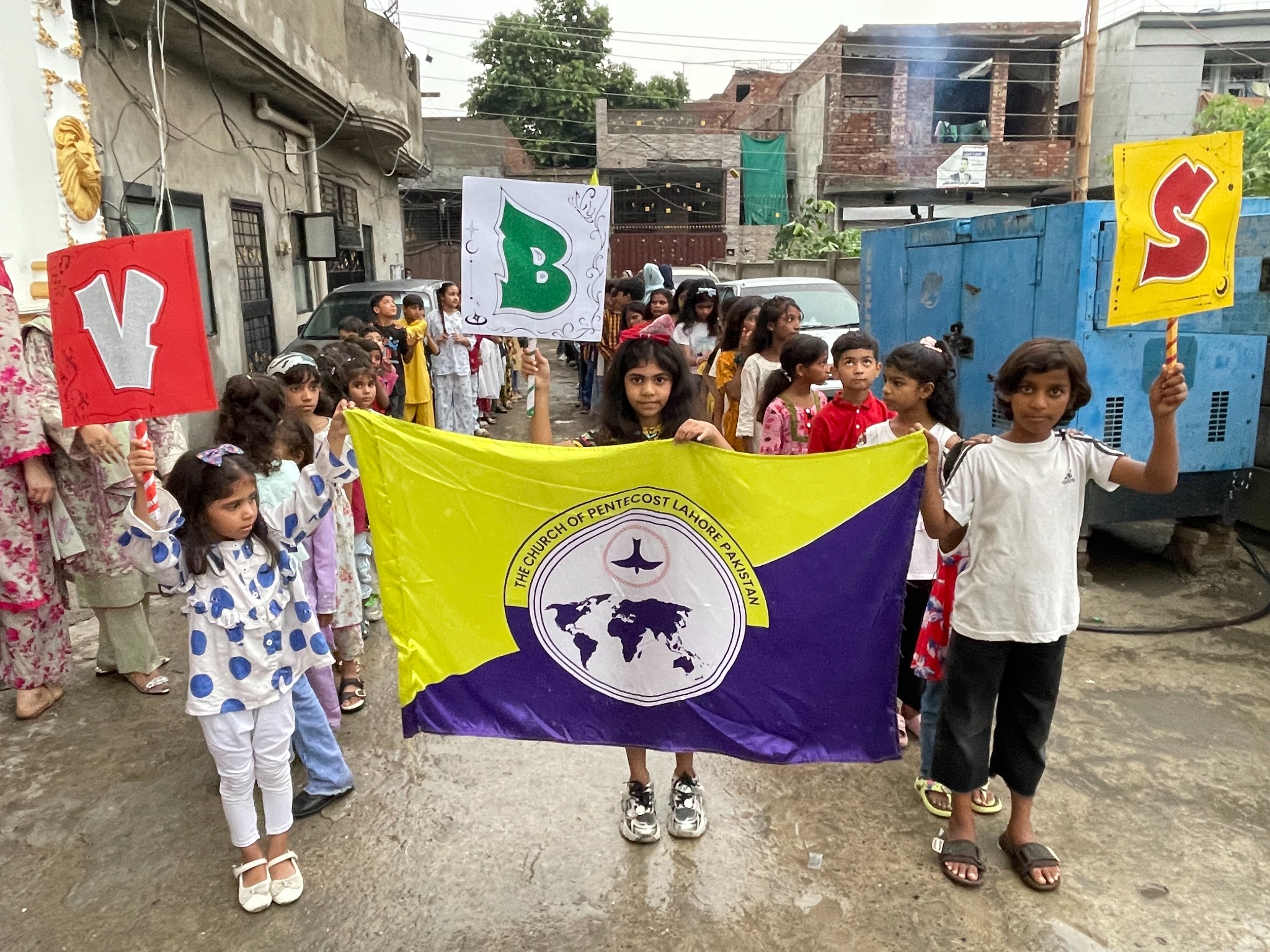Children participating in a community procession with VBS signs.